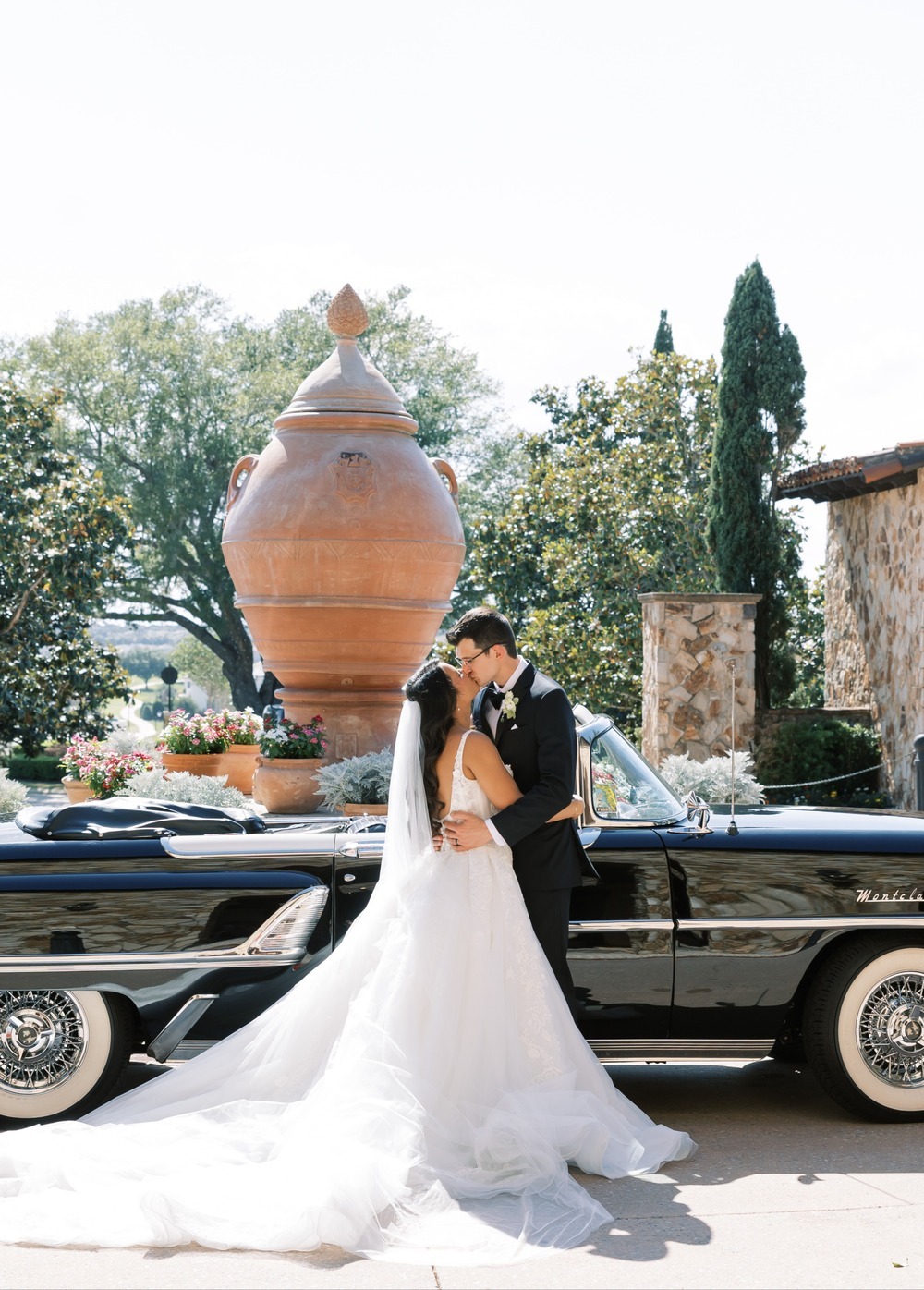 Bride and groom embracing by vintage convertible