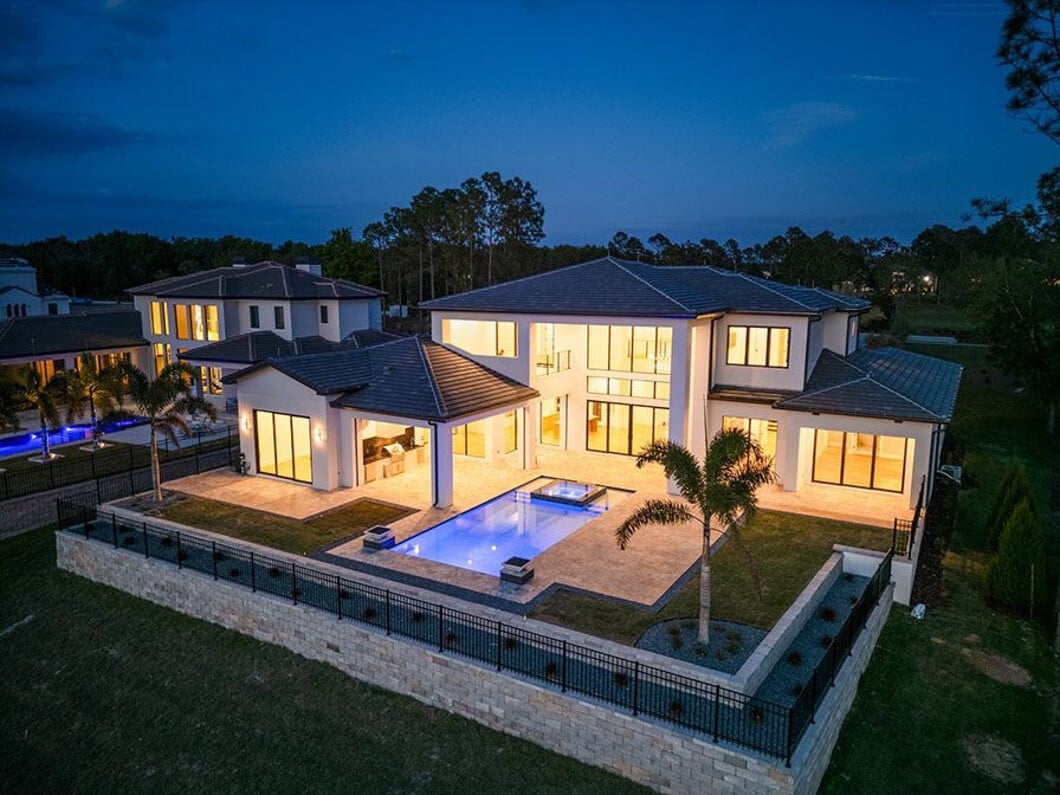 Aerial view of a luxury Bella Collina home with illuminated pool and outdoor living area at dusk