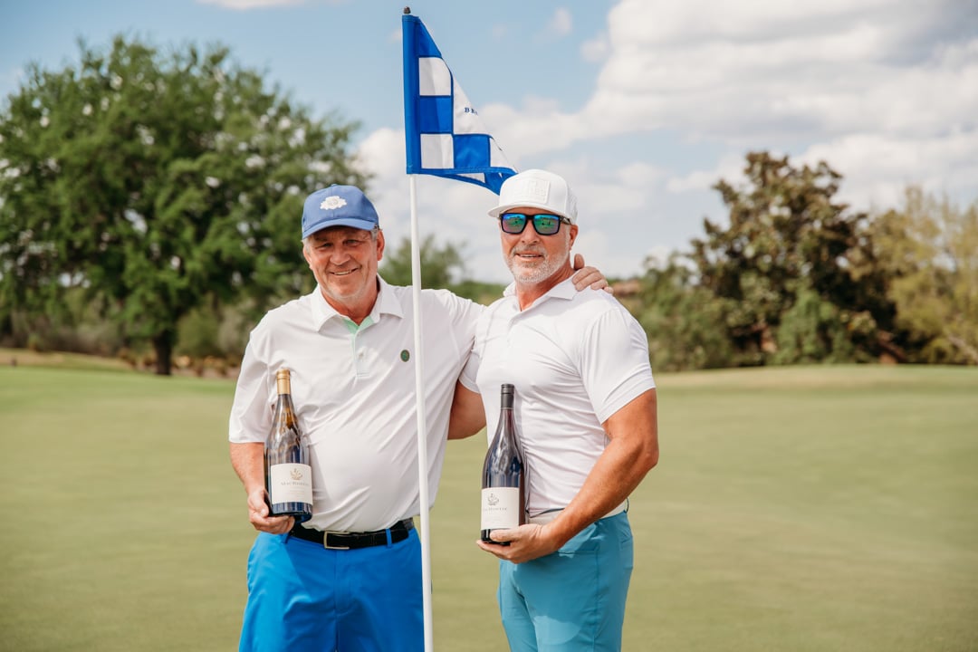 2 males posing at Bella Collina golf hole flag