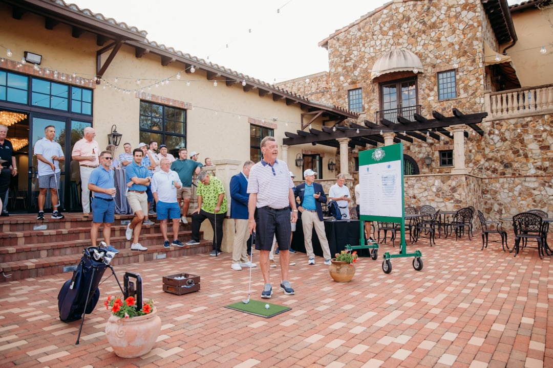Group watching man hitting golf shot at Bella Collina event