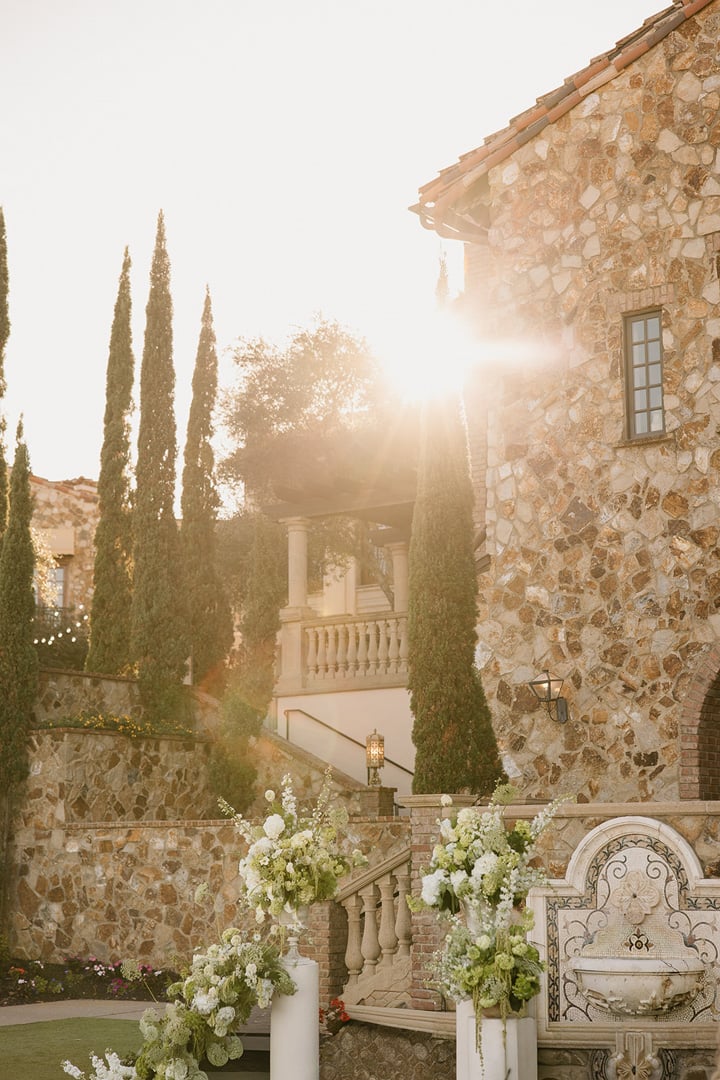 Sunlit stone Clubhouse and floral wedding ceremony setup at Bella Collina