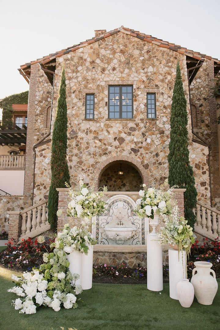 Floral wedding ceremony backdrop in front of the stone Clubhouse at Bella Collina