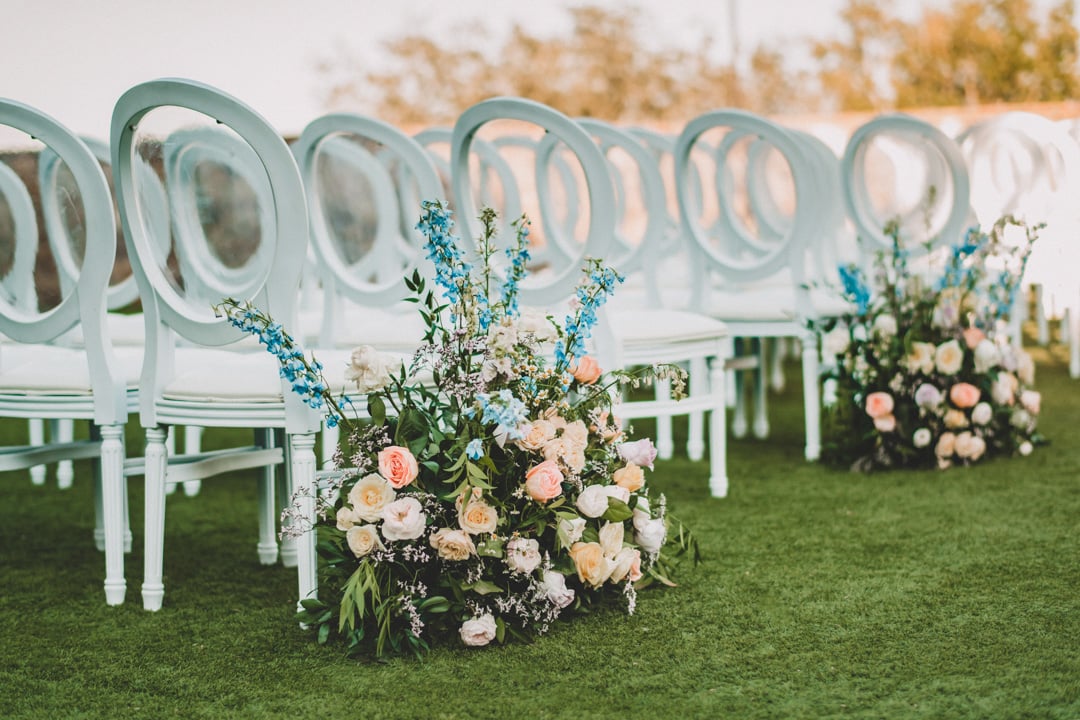 Floral aisle arrangements beside white chairs at an outdoor Bella Collina wedding ceremony