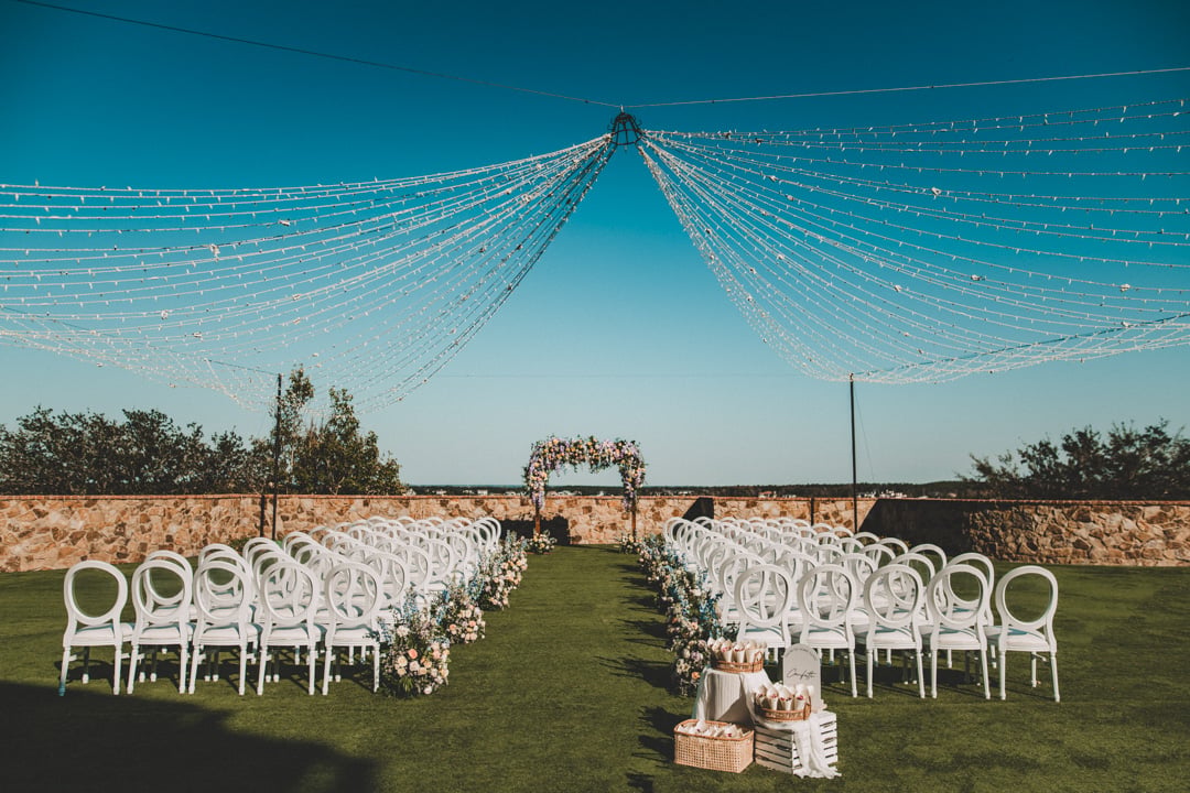 Outdoor wedding ceremony setup with white chairs and overhead string lights at Bella Collina