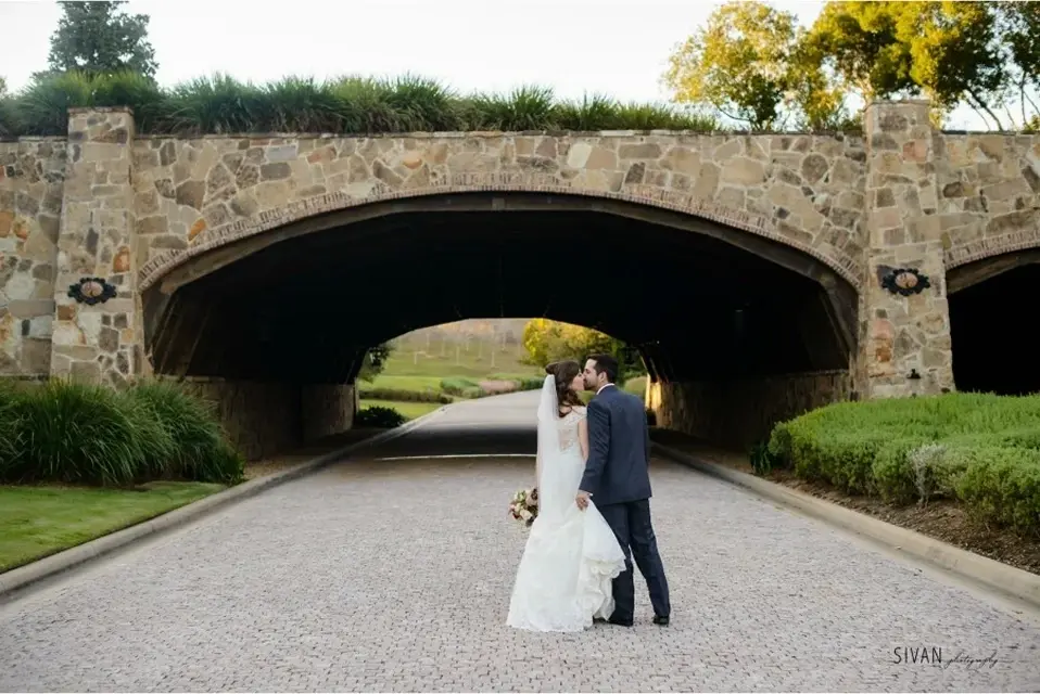 Bride and groom posing beneath at stone bridge at Bella Collina