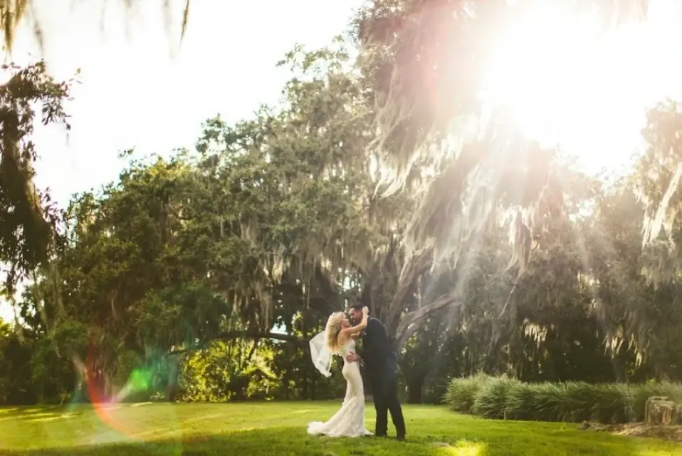 Bride and groom embracing beneath sunlit oak trees at Bella Collina