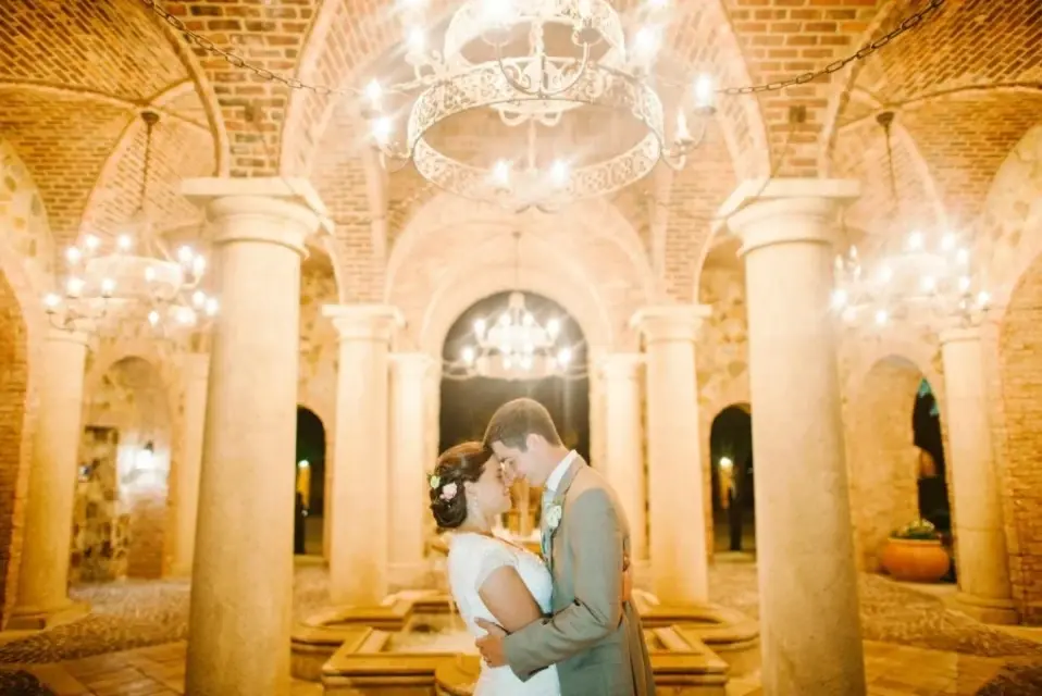 Bride and groom kissing beneath chandeliers in the Bella Collina atrium