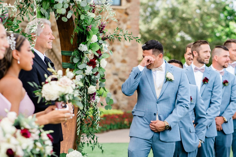 Groom wipes away tears as the bride approaches during an outdoor wedding ceremony at Bella Collina