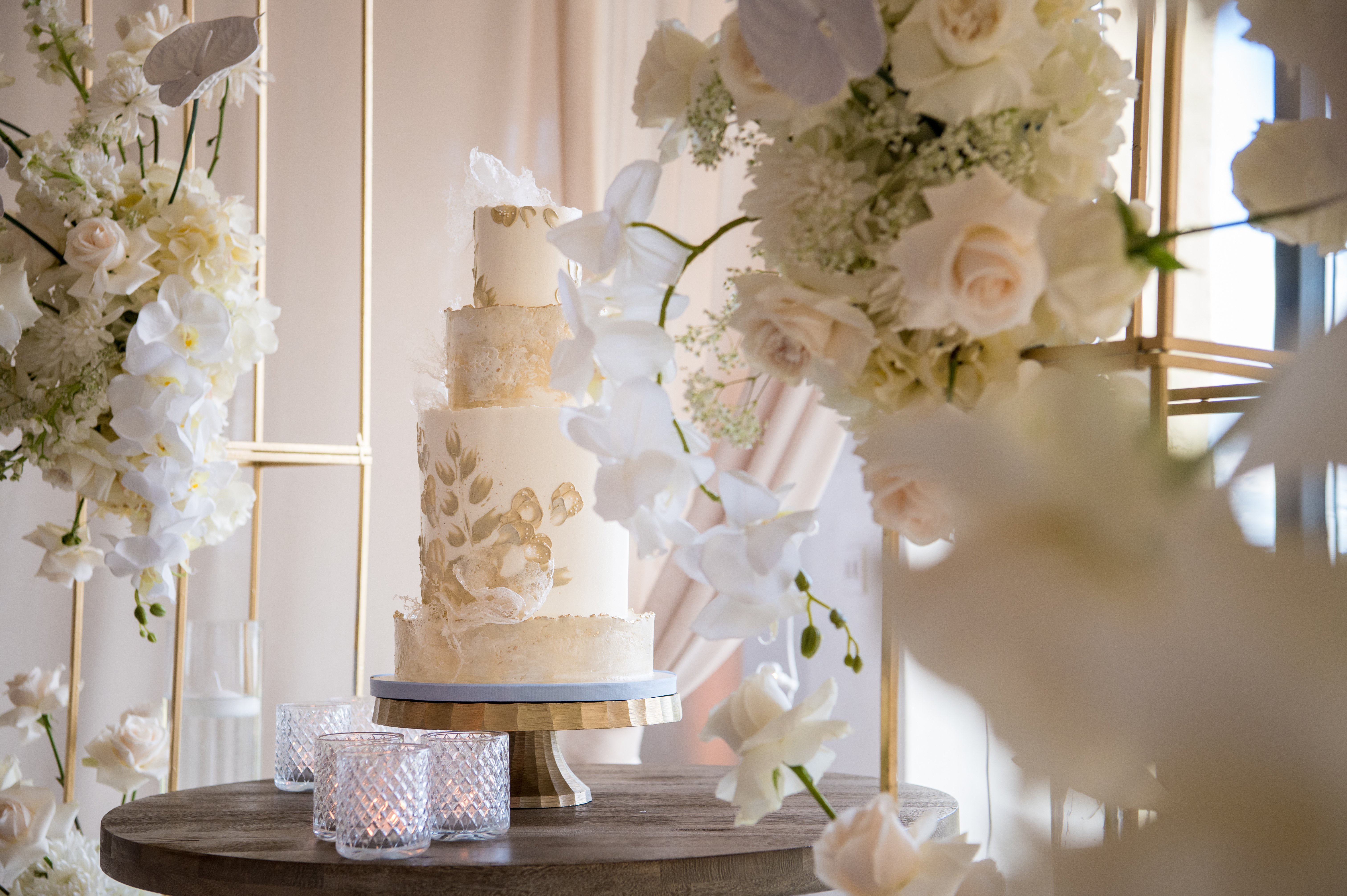 Elegant white wedding cake surrounded by floral arrangements at Bella Collina