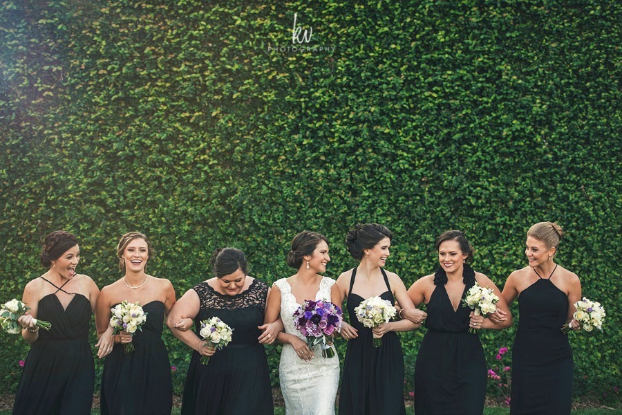 Bride and bridesmaids holding bouquets in front of an ivy-covered wall at Bella Collina