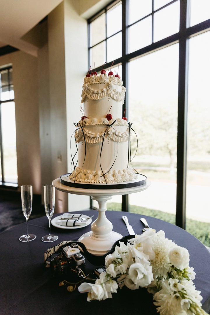 Three-tier white wedding cake with gold detailing and floral accents at Bella Collina