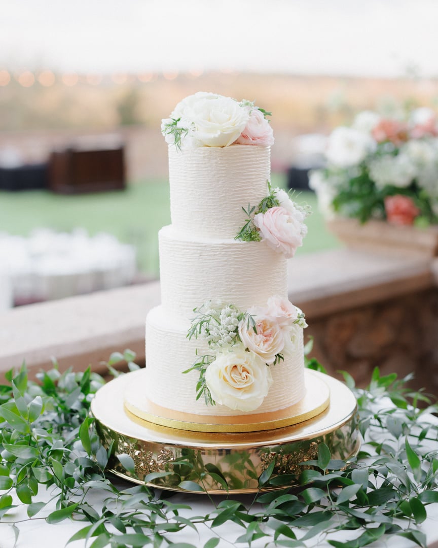 Three-tier white wedding cake with delicate green floral accents at Bella Collina