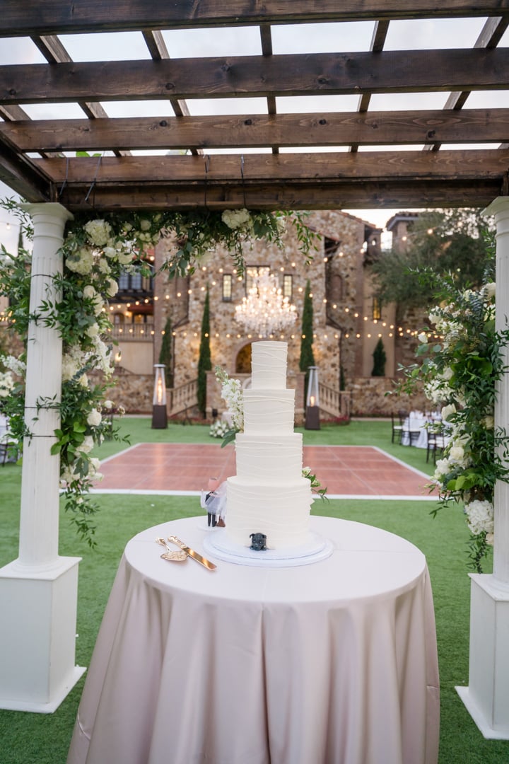 White wedding cake displayed beneath a pergola in the Bella Collina atrium
