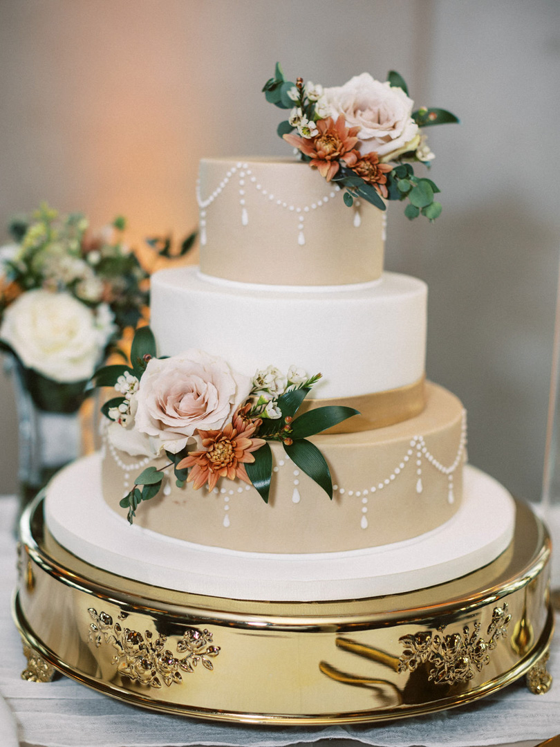 Three-tier white wedding cake with blush roses and greenery at Bella Collina