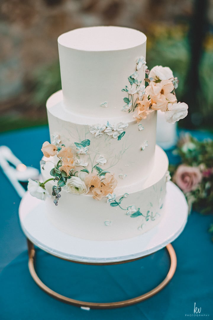 Three-tier white wedding cake with delicate blue and peach floral details at Bella Collina