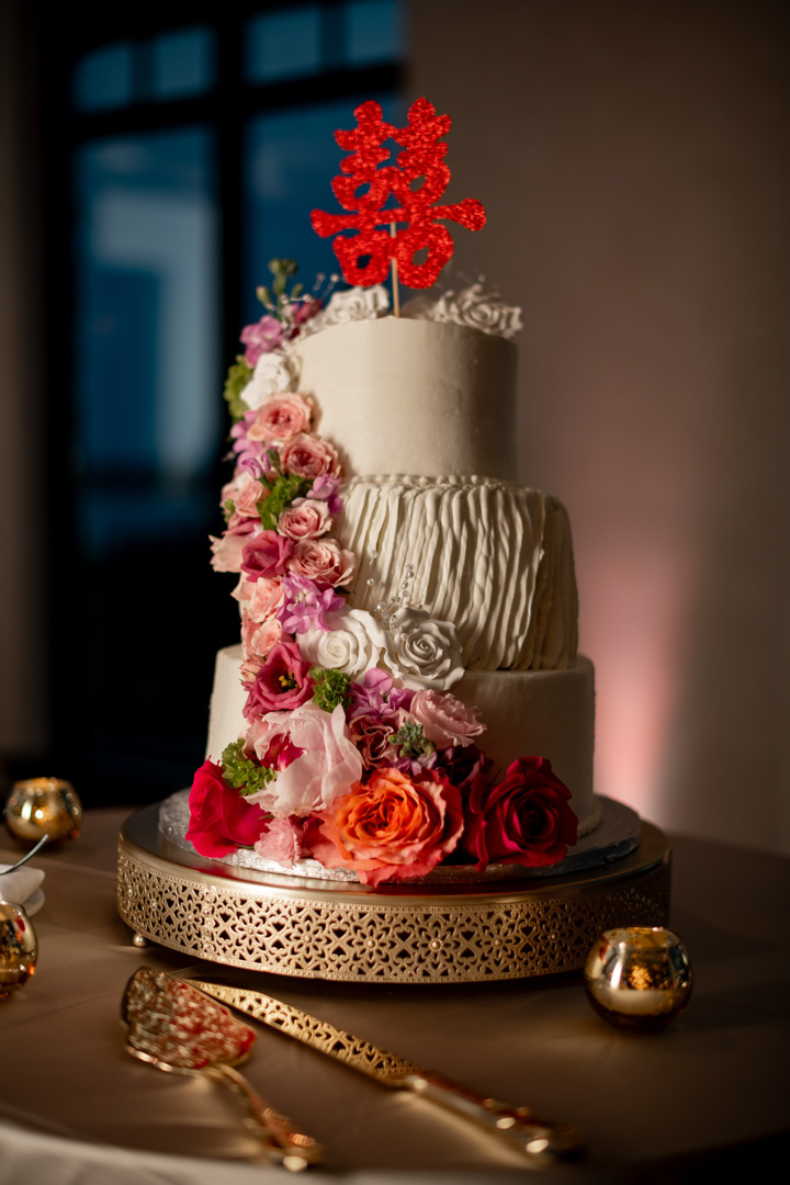 Three-tier wedding cake with cascading pink and red flowers at Bella Collina